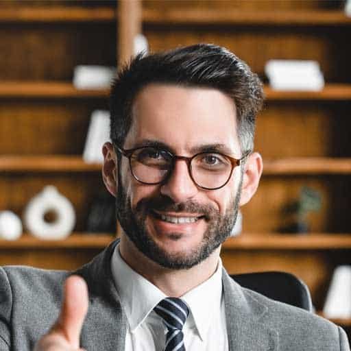 Professional man in glasses smiling, giving a thumbs-up in an office setting.