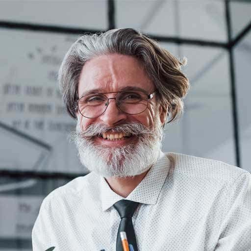 Friendly professional man with gray hair and beard, wearing glasses and a white shirt.